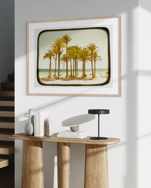 Modern interior with a wooden table, lamp, and framed picture of palm trees.