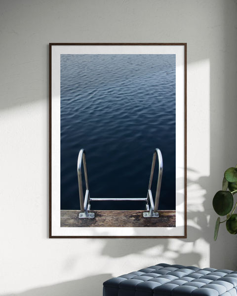A framed wall art print showing a dark blue body of water with metal ladder rails at the bottom.